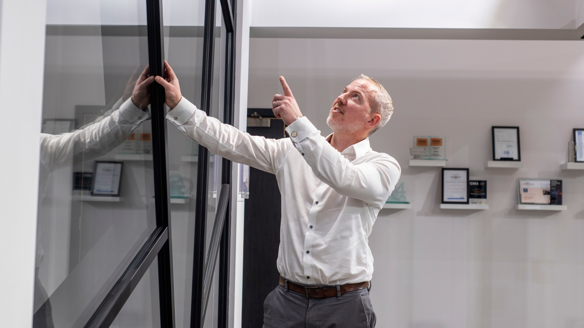 A man stood pointing up at a large glass facade in a showroom
