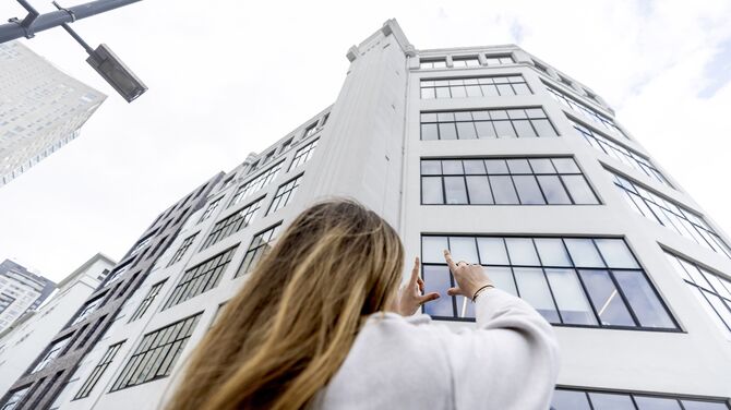Woman holding up her hands towards a white mid-rise building with lots of windows.