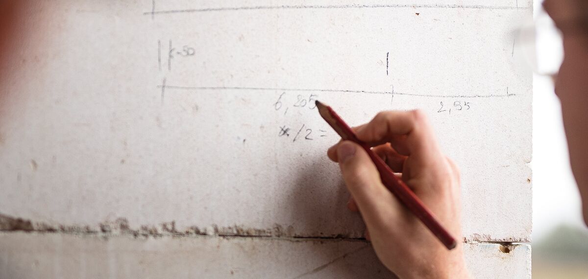 Man writing with pencil on concrete wall of construction site.