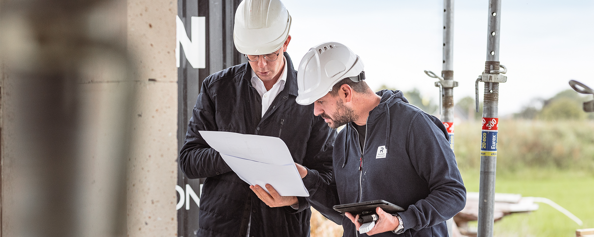 Two men on a building site looking at a piece of paper