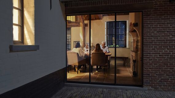 Family sitting at table behind large window at night.