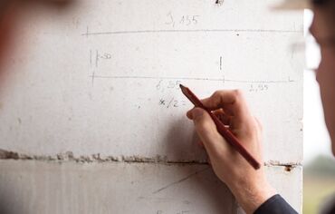 Man writing with pencil on concrete wall of construction site.